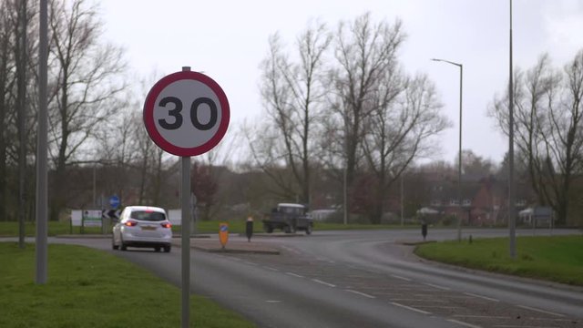 Speed limit sign with traffic passing in the background in England.