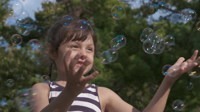 Touch soap bubbles. Happy little girl playing with soap bubbles on a sunny day.