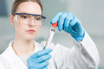 Female scientist with medical gloves and safety glasses is handling a blood probe in a test tube 