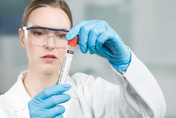 Female scientist with medical gloves and safety glasses is handling a blood probe in a test tube 