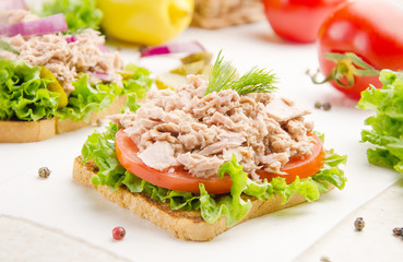 Tuna sandwiches with lettuce tomatoes and onions on parchment paper