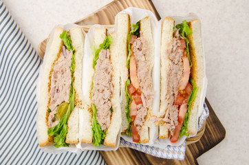Flat lay view at wrapped Tuna sandwiches with lettuce tomatoes pickles and onions in wicker basket...