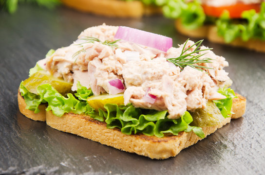 Tuna sandwiches with lettuce tomatoes pickles and onions on slate