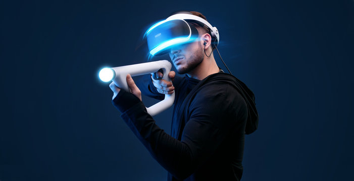 Beautiful man over dark background. Gamer guy in glasses of virtual reality with controllers in hands. Augmented reality, game, hobby concept. VR. Blue neon light. Free space for text.