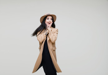 Beautiful girl on gray background. Portrait of charming lady in beige classic coat, hat and black dress. Free space for text.
