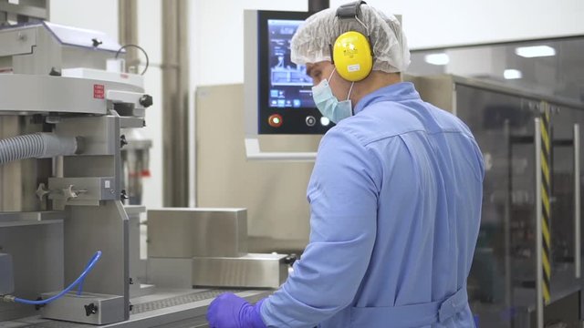 American man engineer working with computer and equipment in modern pharmaceutical company. Back view of employee looks at screen and controls metal facilities in pharma chemical factory. Concept