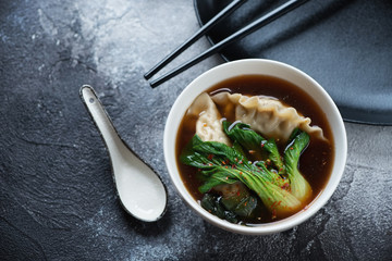 Miso soup with dumplings and pak-choi served in a white bowl, high angle view over grey stone background with space