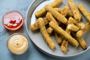 Closeup of breaded chicken sticks on a grey plate with dipping sauces, selective focus