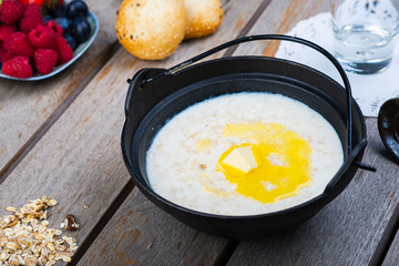 Traditional breakfast milk porridge with butter and berries on a wooden table.