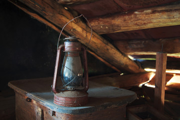 Fototapeta na wymiar Rarity dusty kerosene lamp stands on the old trunk under the ceiling in an old rustic attic, selective focus, space for text