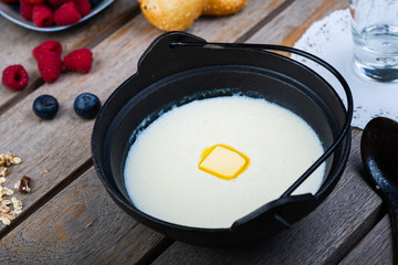 Traditional breakfast milk porridge with butter and berries on a wooden table.