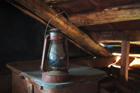 Rarity dusty kerosene lamp stands on the old trunk under the ceiling in an old rustic attic, selective focus, space for text