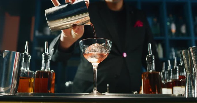 A professional bartender is preparing an alcoholic cocktail with ice cubes to customers at the bar or disco club.