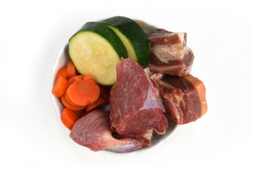 Top view of dog bowl filled with mixture of biologically appropriate raw food containing meat chunks and vegetables isolated on white background