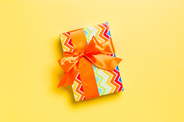 wrapped Christmas or other holiday handmade present in paper with orange ribbon on yellow...
