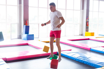 Fototapeta na wymiar Fitness, fun, leisure and sport activity concept - Handsome happy man jumping on a trampoline indoors