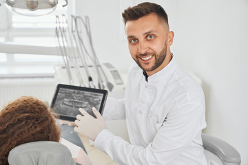 Fototapeta premium Positive male dentist posing while consulting female patient