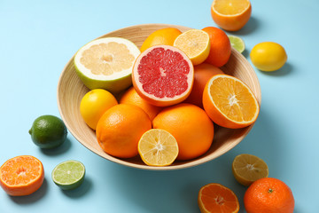 Citrus fruits and bowl on light blue background, close up