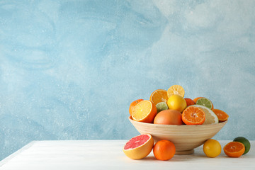 Juicy citrus fruits in bowl on wooden table against blue background, space for text - Powered by Adobe