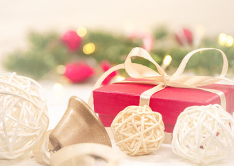 Christmas background, with a red gift box and wicker white balls, on a background of bokeh and green firs in pastel colors.