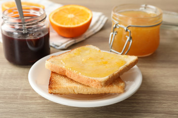 Toasts on plate, jam, towel and orange on wooden background, close up