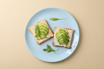 Plate with toasts with avocado, arugula and sesame on beige background, top view