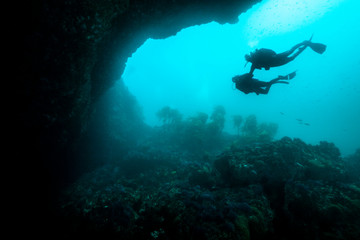 A couple of scuba divers exploring  an underwater arch.