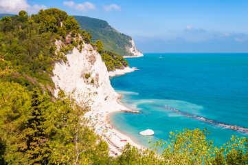 Beautiful coastline of Numana, Ancona, Italy surrounded by high massive white limestone rocky cliffs eroded by Adriatic sea waves and wind. Green pines growing on the rocky mountains.