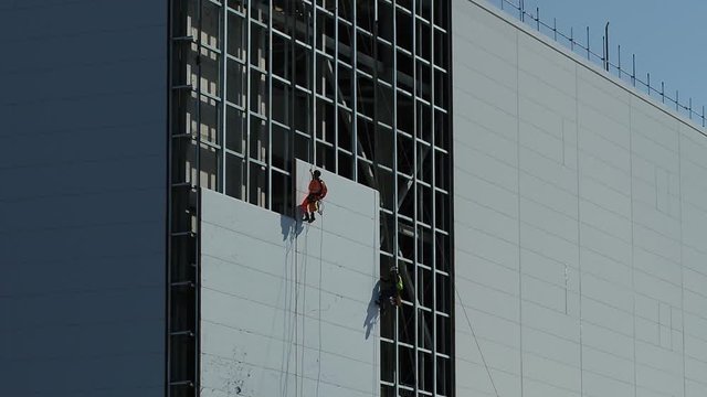 Aerial view of abseiling construction workers, cladding the face of a power station build.