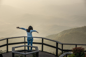 Asian woman looking out over the mountains (golden light background) on Kew Mae Parn at Inthanon National Park mountain in Thailand