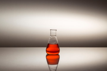 Scientific laboratory glass erlenmeyer flask filled with red liquid on reflective surface.