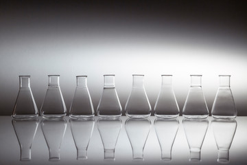 Group of scientific laboratory glass erlenmeyer flask glassware equipment on reflective surface.
