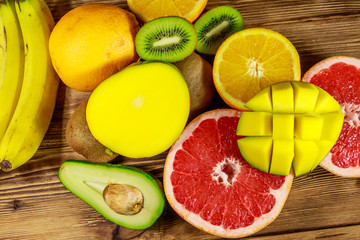 Assortment of tropical fruits on wooden table. Still life with bananas, mango, oranges, avocado, grapefruit and kiwi fruits