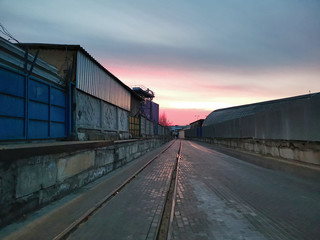 Obraz premium Widok na długą drogę między magazynami. Czerwone słońce świt.