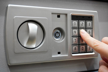 the man dials the code to close the safe. Grey safe closure, numeric keypad. A man presses the keys on the digital panel on the safe.