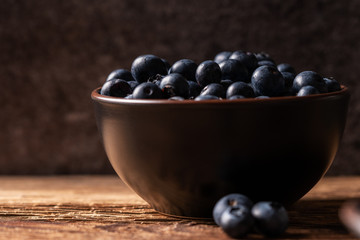 Fresh ripe blueberries in brown ceramic bowl on wooden table with dark background, ingredients for healthy diet lifestyle concept, dark and moody, frontal head-on view, horizontal format
