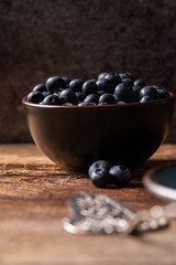 Fresh ripe blueberries in brown ceramic bowl on wooden table with dark background, ingredients for healthy diet lifestyle concept, dark and moody, eye level view, vertical format