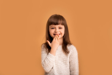 Little cute girl laughs after hearing a funny joke and closes her mouth with her hand, shy of her...