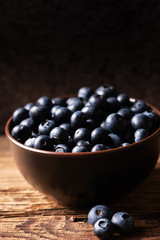 Fresh ripe blueberries in brown ceramic bowl on wooden table with dark background, ingredients for healthy diet lifestyle concept, dark and moody, 45 degree angle view, vertical format, copy space