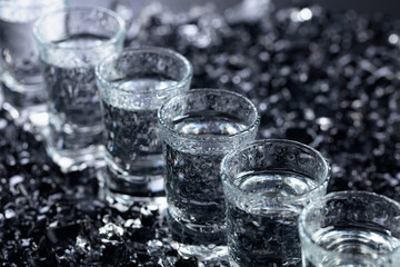 Damp glasses of vodka with ice on a black reflective background.