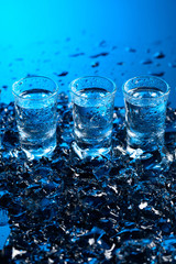 Damp glasses of vodka with ice on a black reflective background.