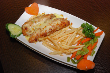 Fried chicken fillet under cheese with french fries and fresh vegetables on the white plate