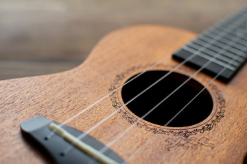 Close-up brown ukulele strings, soundhole, bridge and neck on brown wooden background. Music...