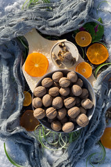 flat lay with  walnut on wooden board,   cracked nut with nutshell, ebony, mandarin, green grass, gray scarf on background
