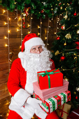 Fototapeta na wymiar Merry Christmas. Santa Claus near Christmas tree with gifts and lights