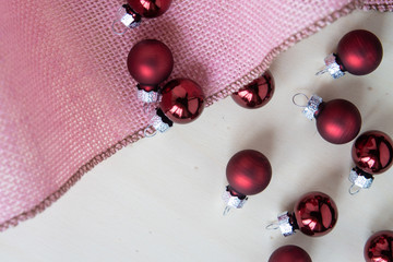 rote Christbaumkugeln zu Weihnachten mit rosa Stoff auf Untergrund aus Holz