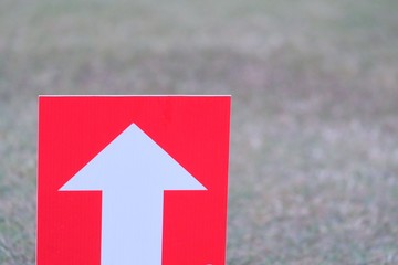 White arrow icon direction on red board with blurred ground field