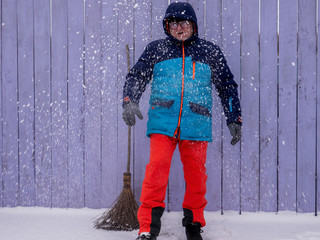 man in bright ski suit stands holding broom in his hands and is going to clean the snow in winter...