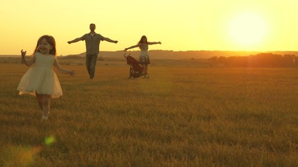 Fototapeta na wymiar Happy child and parents walk at sunset. Dad hugs daughter and whirls in flight. Silhouette of a family walking in the sun. Mom dad and baby. The concept of a happy family. Family lifestyle.