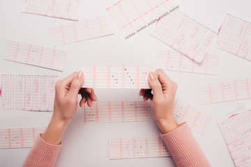 cropped view of woman holding lottery ticket with marked numbers near scattered lottery cards on white table